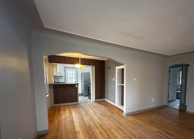 interior space featuring light wood-style floors, arched walkways, a sink, and baseboards