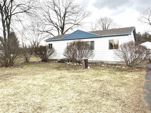 view of side of property with roof with shingles and a yard