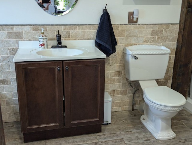 half bath featuring wainscoting, toilet, wood finished floors, vanity, and tile walls