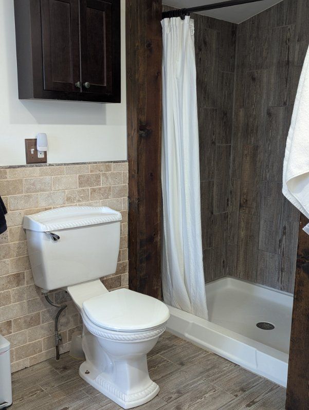 bathroom with a stall shower, tile walls, toilet, and wood finished floors