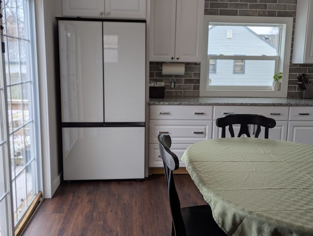 kitchen with dark wood-type flooring, backsplash, freestanding refrigerator, and white cabinets