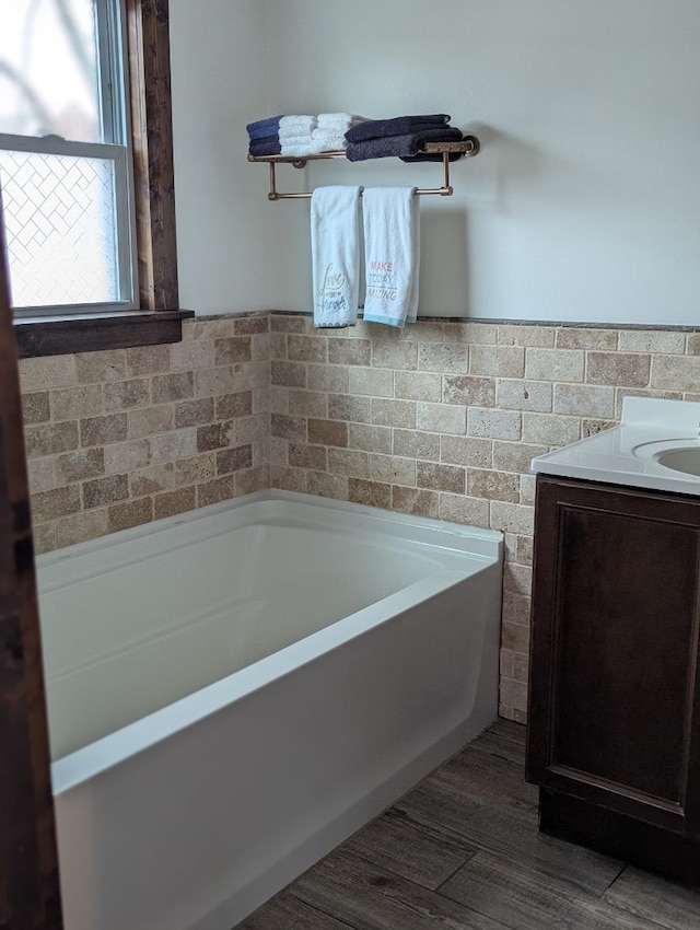 bathroom with tile walls, wainscoting, vanity, wood finished floors, and a bath