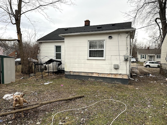 back of house featuring an outbuilding, a storage shed, a chimney, and fence