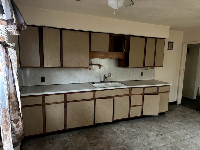 kitchen with light countertops, backsplash, a ceiling fan, a sink, and a textured ceiling