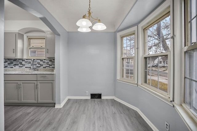 unfurnished dining area with a chandelier, light wood finished floors, a sink, and baseboards