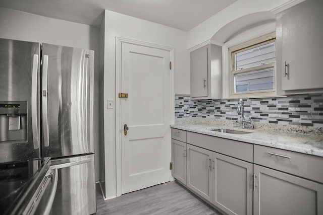 kitchen with light wood-style flooring, gray cabinetry, a sink, appliances with stainless steel finishes, and backsplash