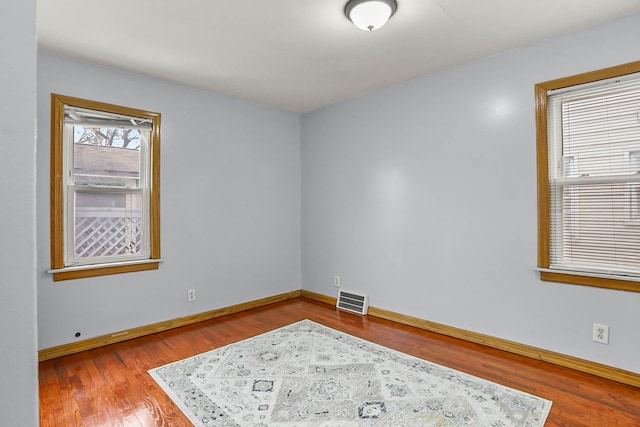 unfurnished room featuring wood finished floors, visible vents, and baseboards