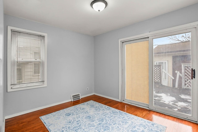 empty room featuring wood finished floors, visible vents, and baseboards