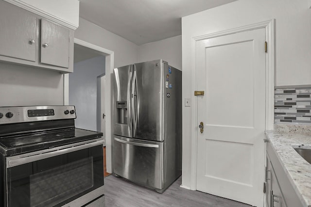 kitchen with stainless steel appliances, tasteful backsplash, light wood-type flooring, and light stone counters