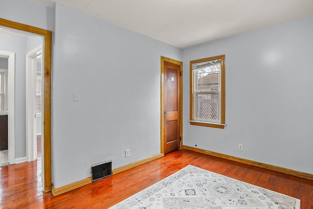 spare room featuring wood-type flooring, visible vents, and baseboards