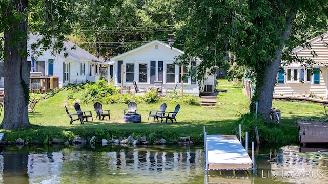 back of property with a water view, a fire pit, and a lawn