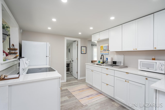 kitchen with white appliances, light wood-style flooring, white cabinets, and a sink