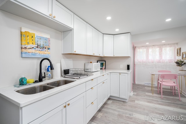 kitchen with white cabinetry, light countertops, a sink, and white microwave