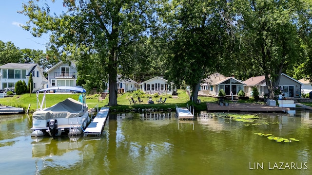 dock area with a water view, boat lift, a residential view, and a yard