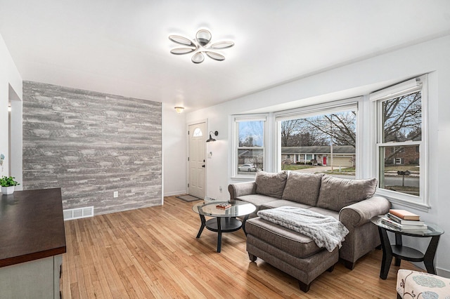 living area featuring wooden walls, light wood-style flooring, an accent wall, and visible vents