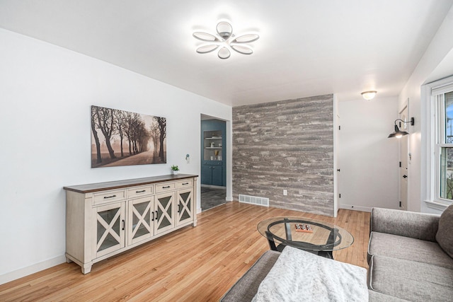 living room with an accent wall, visible vents, light wood-style flooring, and baseboards