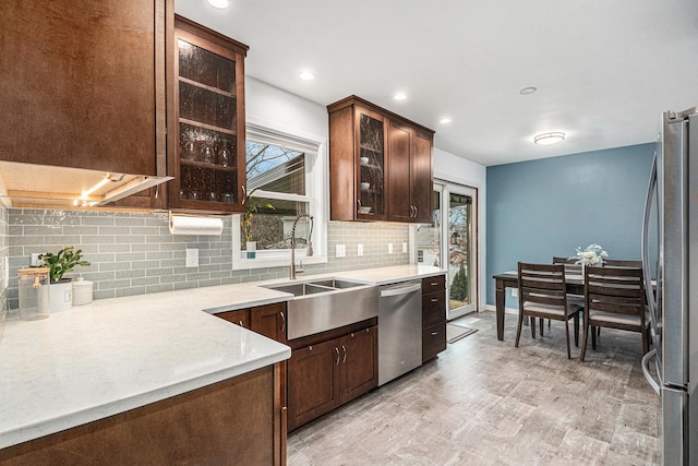 kitchen featuring stainless steel appliances, backsplash, light wood-style floors, a sink, and dark brown cabinets