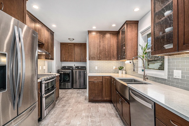 kitchen with decorative backsplash, appliances with stainless steel finishes, a sink, light stone countertops, and independent washer and dryer