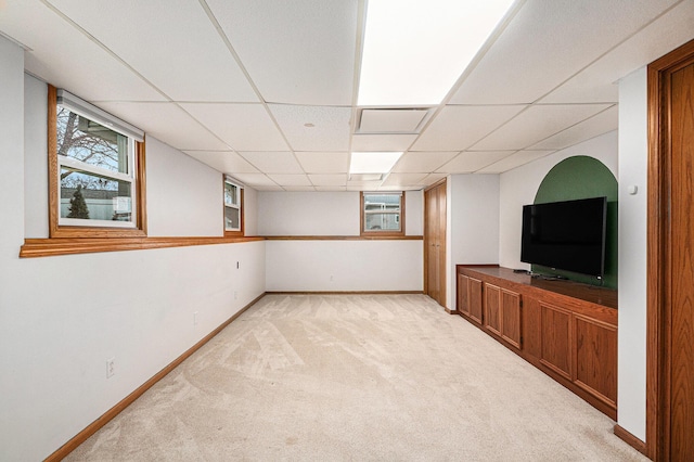 basement featuring a wealth of natural light, a paneled ceiling, light carpet, and baseboards