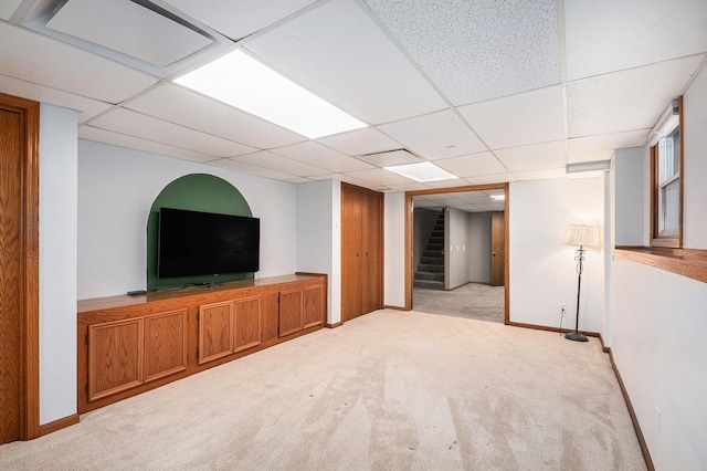 finished basement featuring stairs, light carpet, a paneled ceiling, and baseboards