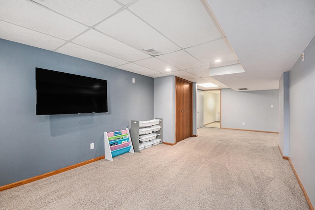 finished below grade area with a paneled ceiling, baseboards, visible vents, and light colored carpet