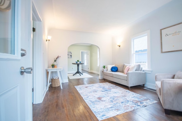 living room with arched walkways, dark wood-style flooring, and baseboards