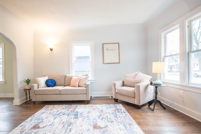 living room featuring arched walkways, dark wood-type flooring, visible vents, and baseboards