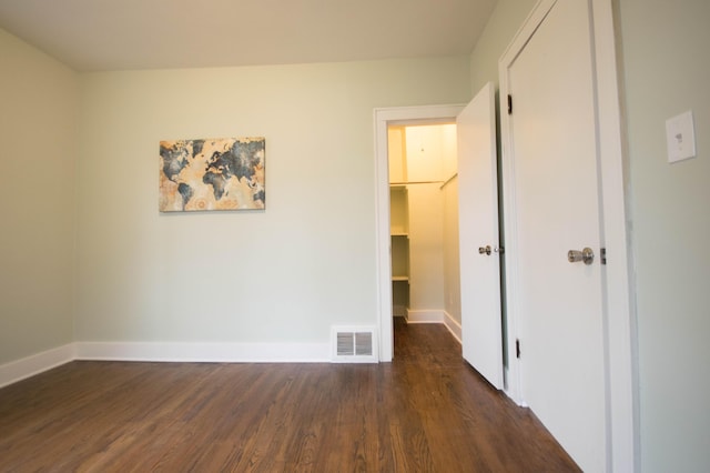 unfurnished bedroom with a walk in closet, dark wood finished floors, a closet, visible vents, and baseboards