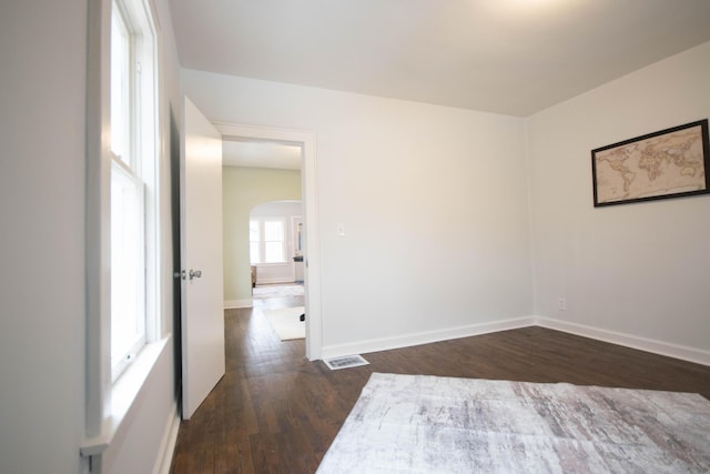 empty room featuring arched walkways, visible vents, dark wood finished floors, and baseboards