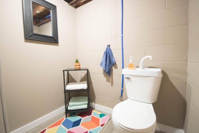 half bathroom featuring toilet, baseboards, and concrete block wall