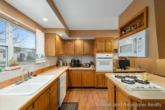 kitchen featuring brown cabinets, white appliances, light countertops, and a sink