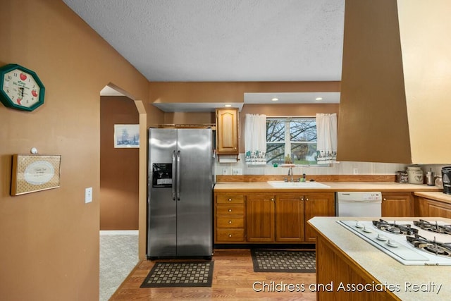 kitchen featuring arched walkways, light countertops, white appliances, and a sink