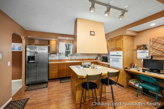 kitchen featuring stainless steel fridge, arched walkways, oven, light countertops, and a sink