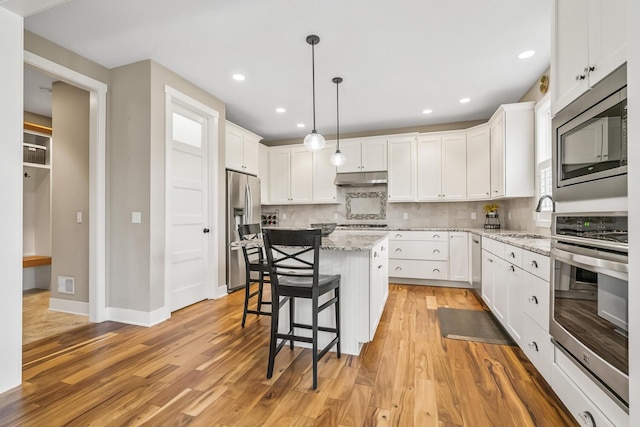 kitchen with a center island, appliances with stainless steel finishes, white cabinets, a sink, and under cabinet range hood