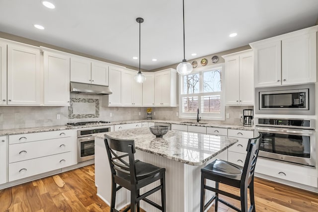 kitchen with appliances with stainless steel finishes, white cabinetry, a sink, under cabinet range hood, and a kitchen breakfast bar