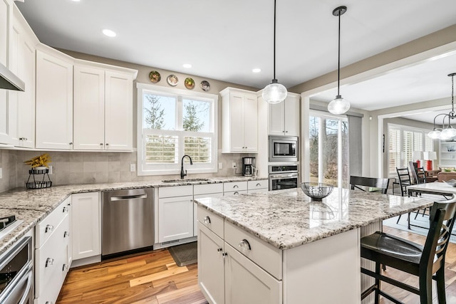 kitchen with a sink, a kitchen breakfast bar, appliances with stainless steel finishes, light wood finished floors, and plenty of natural light