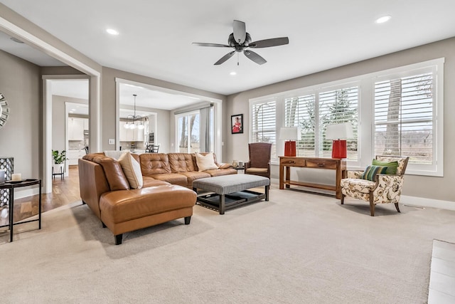 living area with light carpet, ceiling fan with notable chandelier, baseboards, and recessed lighting