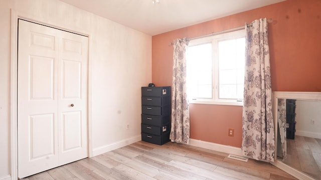 unfurnished bedroom featuring baseboards, a closet, visible vents, and light wood-style floors