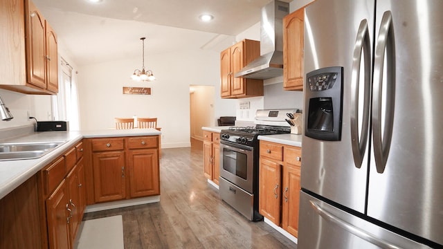 kitchen featuring wood finished floors, vaulted ceiling, stainless steel appliances, wall chimney range hood, and a sink