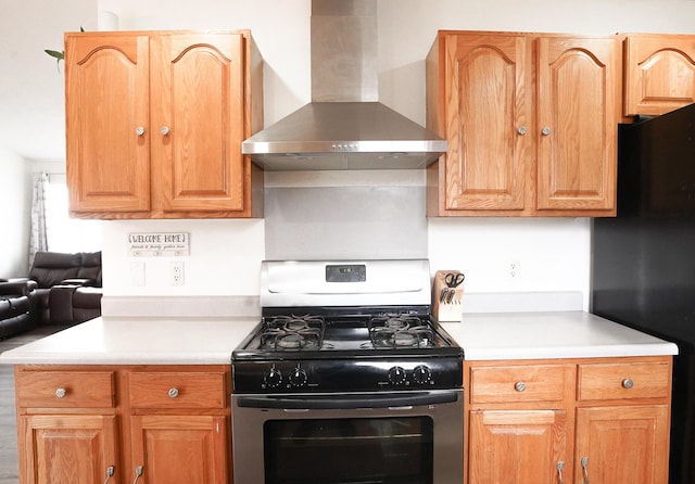 kitchen featuring wall chimney exhaust hood, stainless steel range with gas cooktop, light countertops, and freestanding refrigerator