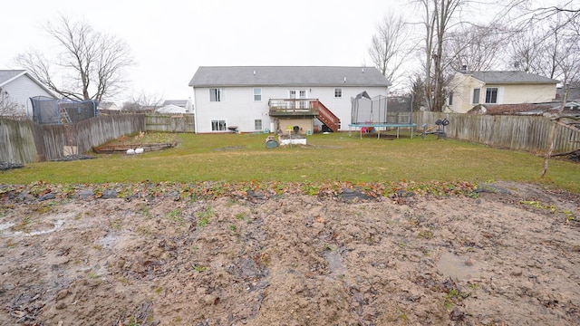 rear view of property featuring a fenced backyard, a trampoline, a lawn, and a wooden deck