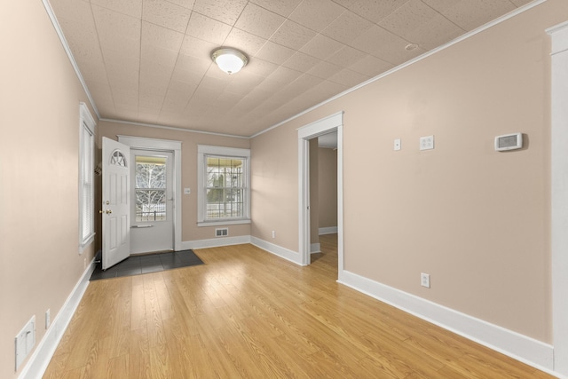 foyer entrance with light wood finished floors, ornamental molding, visible vents, and baseboards