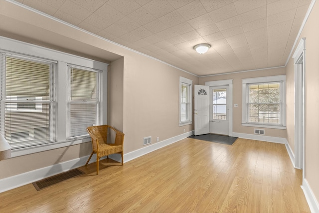 entryway with light wood-style flooring, visible vents, and crown molding