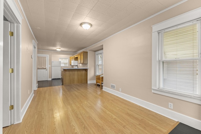 unfurnished living room featuring light wood finished floors, baseboards, visible vents, and crown molding