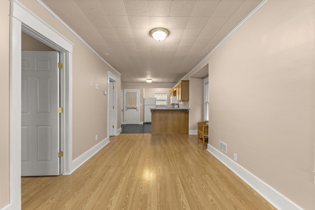 interior space featuring light wood-type flooring, visible vents, crown molding, and baseboards