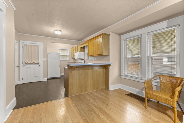 kitchen featuring a peninsula, white appliances, a breakfast bar, wood finished floors, and crown molding