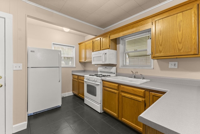 kitchen with crown molding, light countertops, a sink, white appliances, and dark tile patterned floors