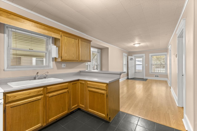 kitchen featuring light countertops, open floor plan, a sink, a peninsula, and baseboards