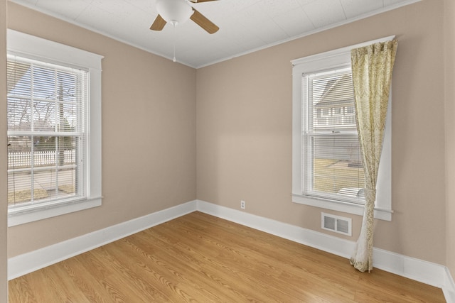 spare room featuring ceiling fan, visible vents, baseboards, ornamental molding, and light wood-type flooring