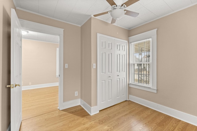 unfurnished bedroom with a closet, baseboards, crown molding, and light wood finished floors